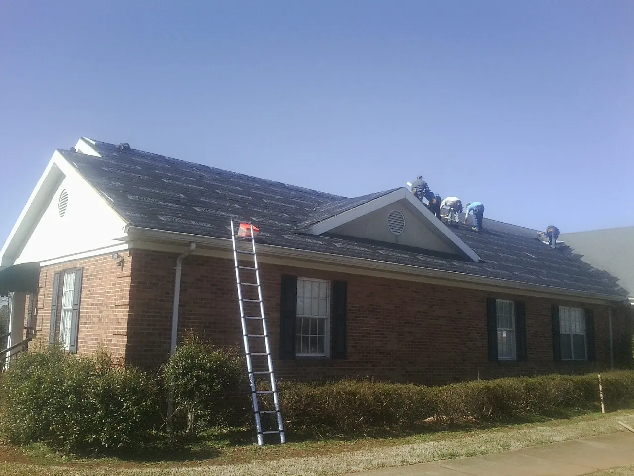 Crew tearing shingles off a brick ranch roof with a ladder set — Emergency Roof Repair work by our crew in Fallston