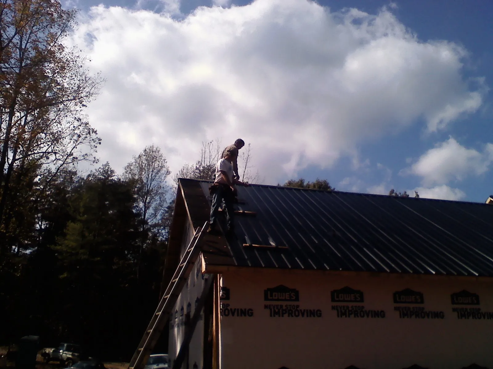 Roofer fastening dark metal panels high against a cloudy sky, from a Roof Inspection job in Fallston